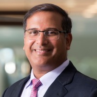 Head-and-shoulders portrait of Falgunbhai Patel in a dark suit against a corporate interior.
